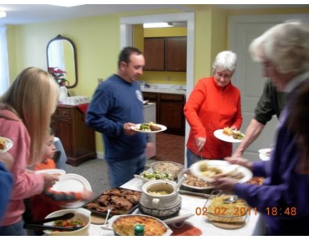 People serving and eating food at a family gathering in a kitchen.