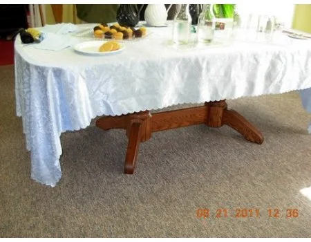 Part of a dining table with a white tablecloth, some plates with food, and drinks, set on a beige carpeted floor.