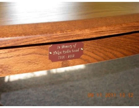 Close-up of a wooden plaque with an engraved message dedicated in memory of a loved one, with a date at the bottom.