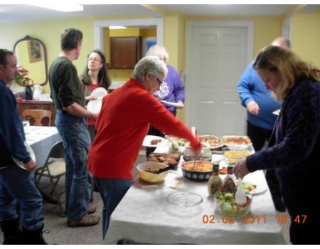 Group of people gathered around a kitchen island serving food at a casual gathering.