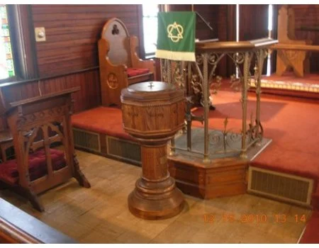 Interior of a church with wooden pews, a wooden pulpit, and a small altar decorated with green fabric.