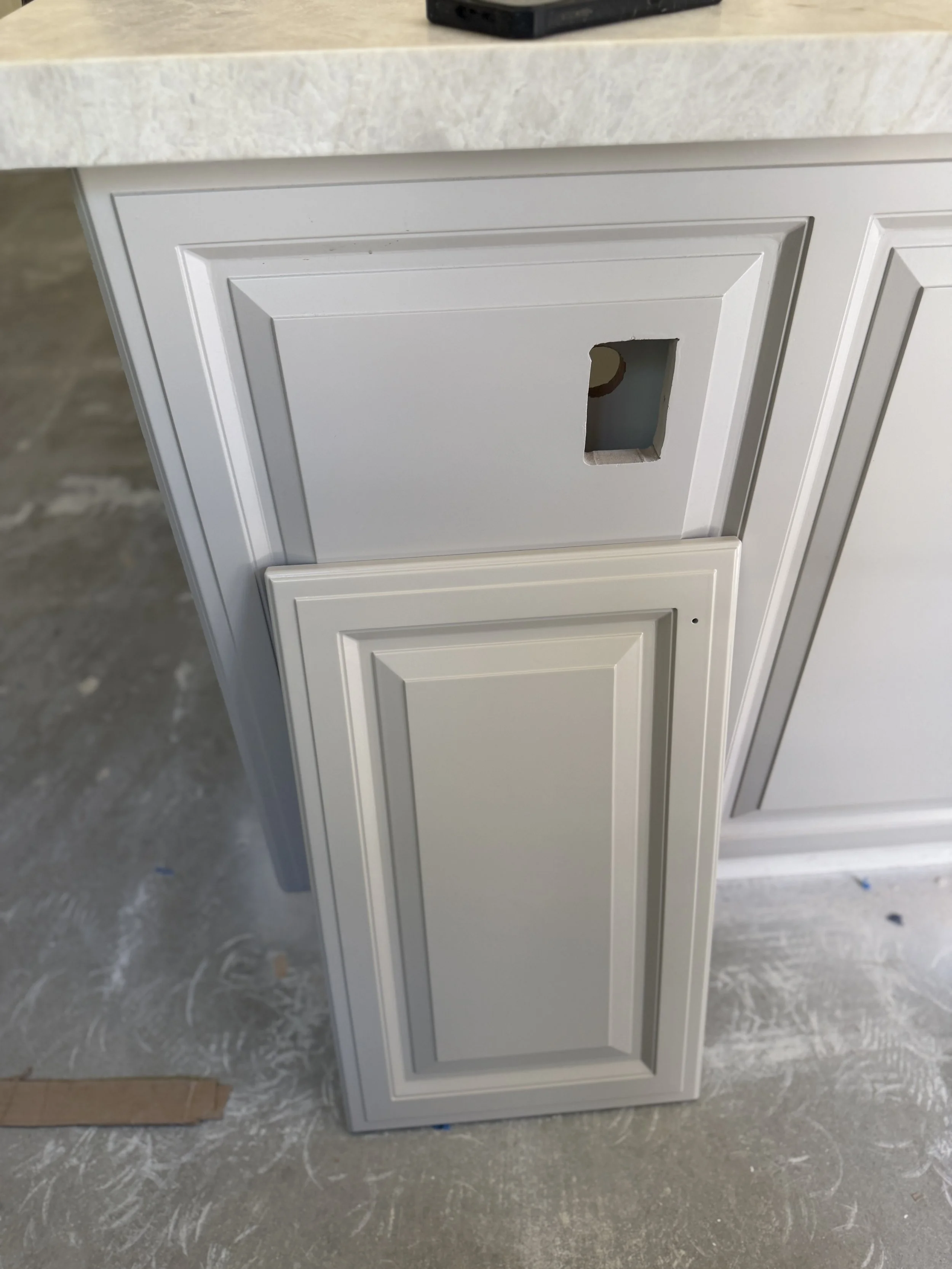 Installed cabinet box and a loose door side by side — the matched paint reads as two different greiges.