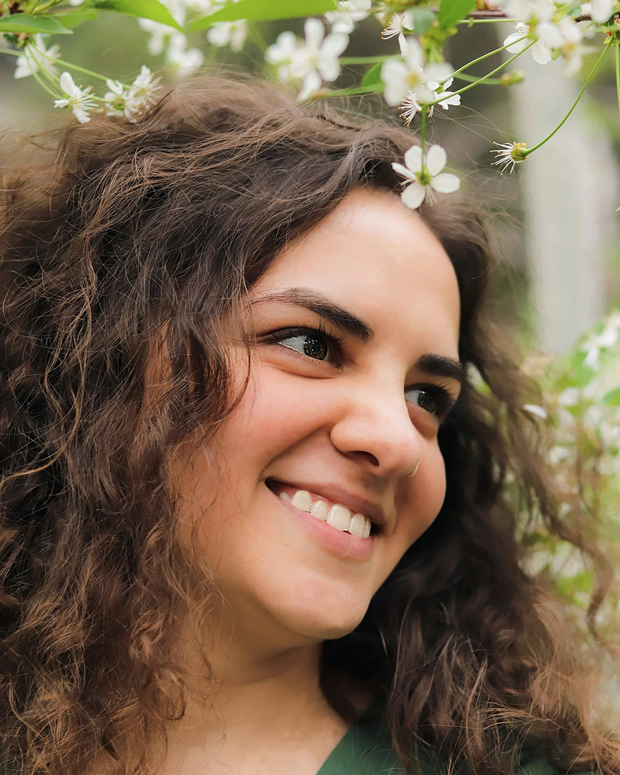 Close-up of a smiling woman with curly hair surrounded by white flowers.