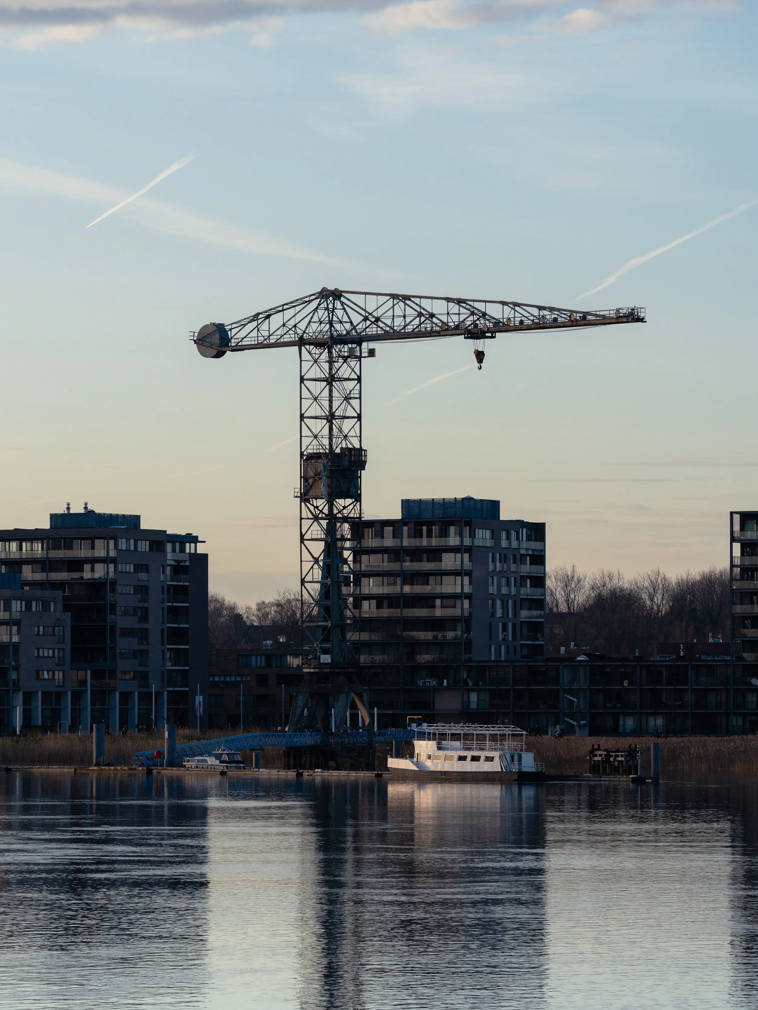 Stalen bouwwerk en woonboten aan een rivier, met moderne appartementen erachter.