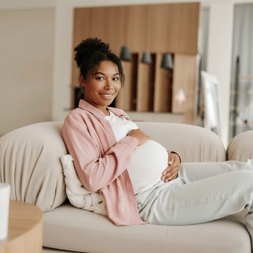 Pregnant woman smiling and relaxing on a sofa in a living room.