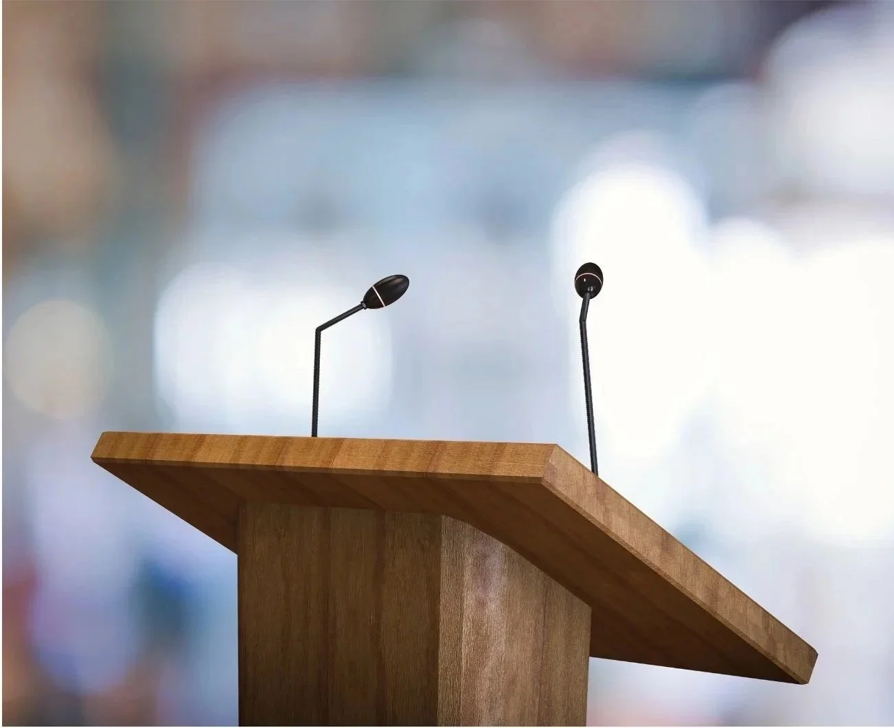 Empty wooden podium with two microphones on stands, blurred background.