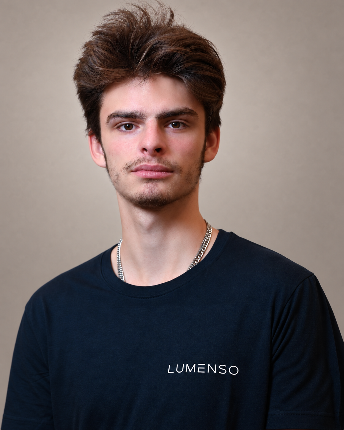 Ein junger Mann mit kurz geschnittenem Haar trägt ein schwarzes T-Shirt mit dem Logo »LUMENSO". Er lächelt und schaut in die Kamera, vor einem weißen Hintergrund.