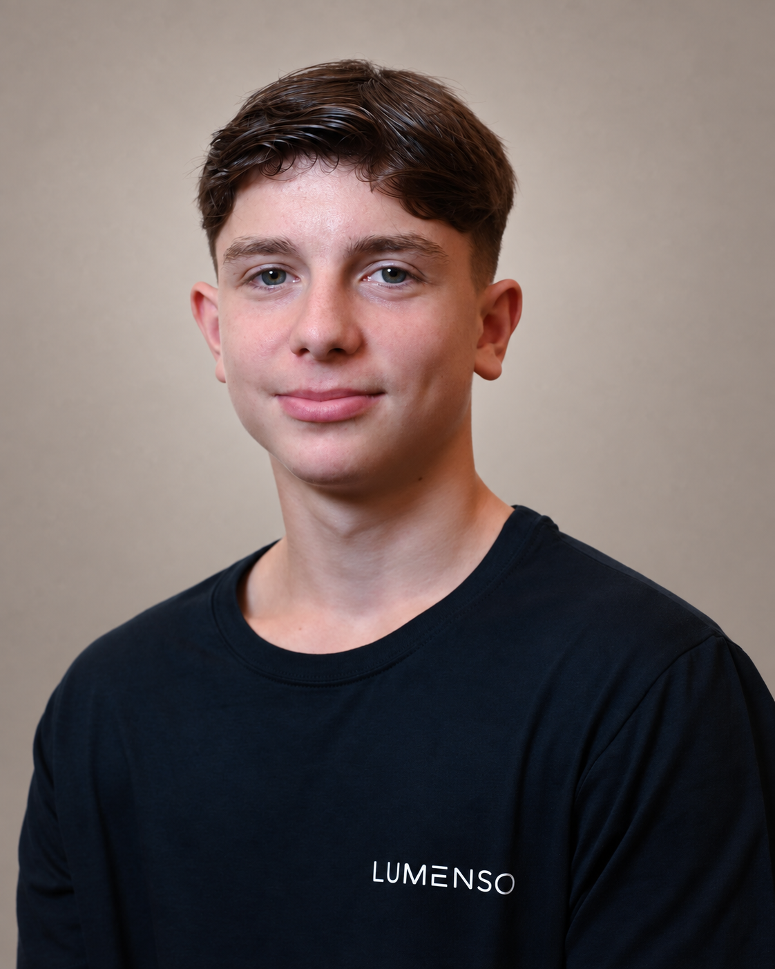 Junger Mann mit kurzem hellem Haar und leichtem Schnurrbart, trägt schwarzes T-Shirt mit Logo 'LUMENSO', blickt lächelnd in die Kamera vor hellem Hintergrund.