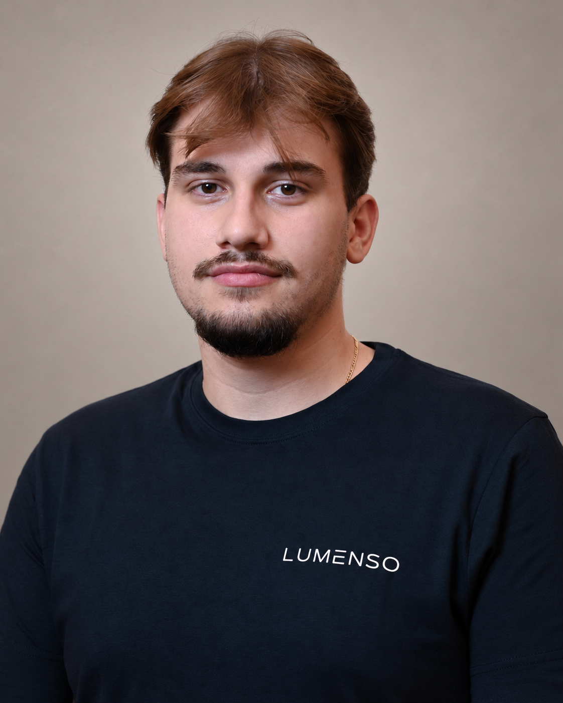 Junger Mann mit kurzem braunem Haar und leichtem Schnurrbart, trägt schwarzes T-Shirt mit Logo 'LUMENSO', blickt lächelnd in die Kamera vor hellem Hintergrund.