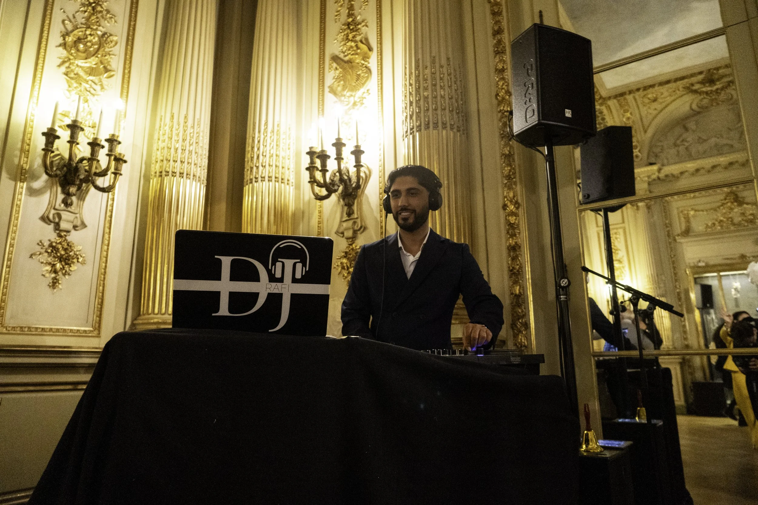 Ein DJ mit Kopfhörern hinter einem DJ-Pult in einem eleganten, goldverzierten Raum, der bei einer Veranstaltung auflegt.