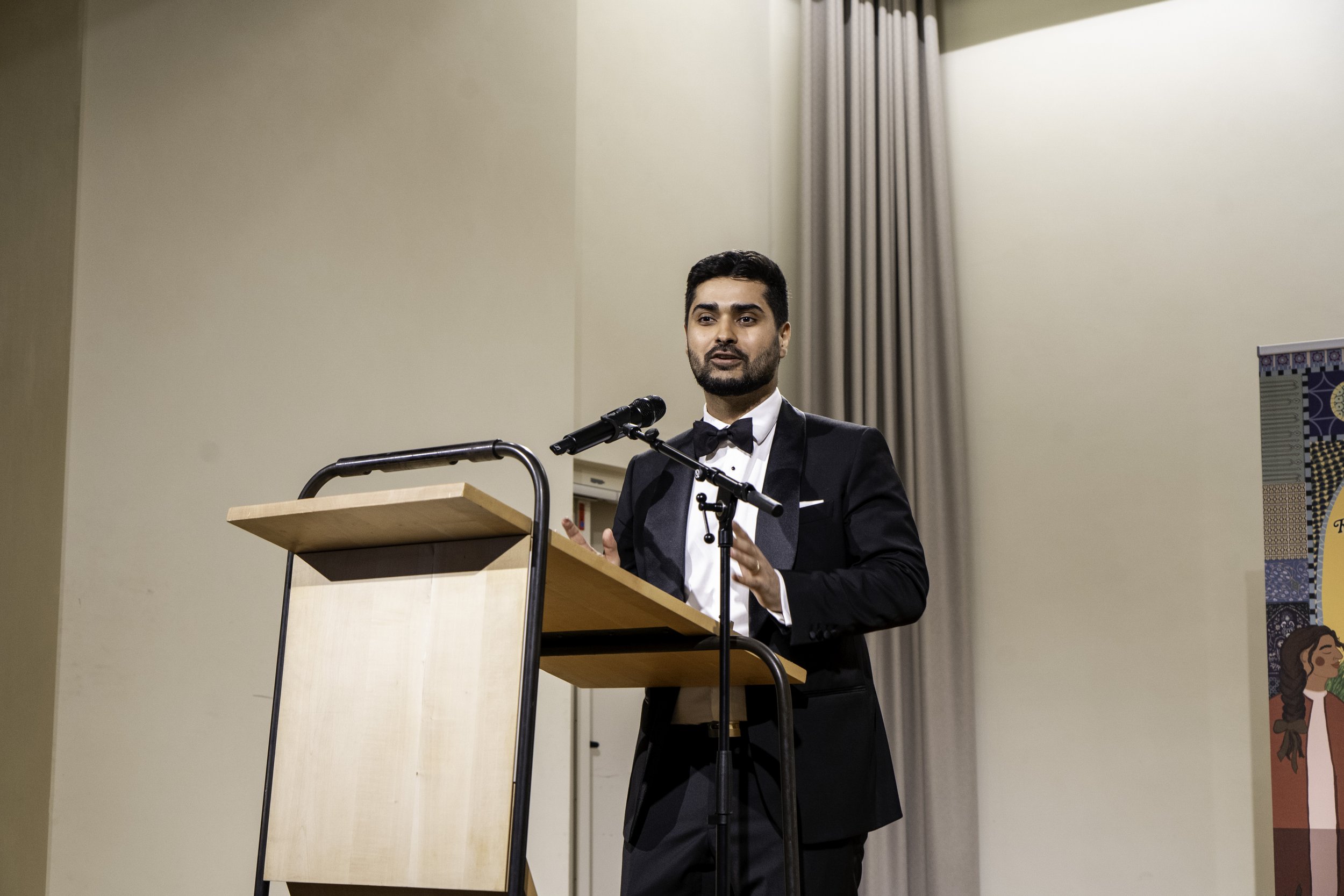 Mann in Gala Kleidung steht hinter einem Rednerpult und spricht vor Publikum.