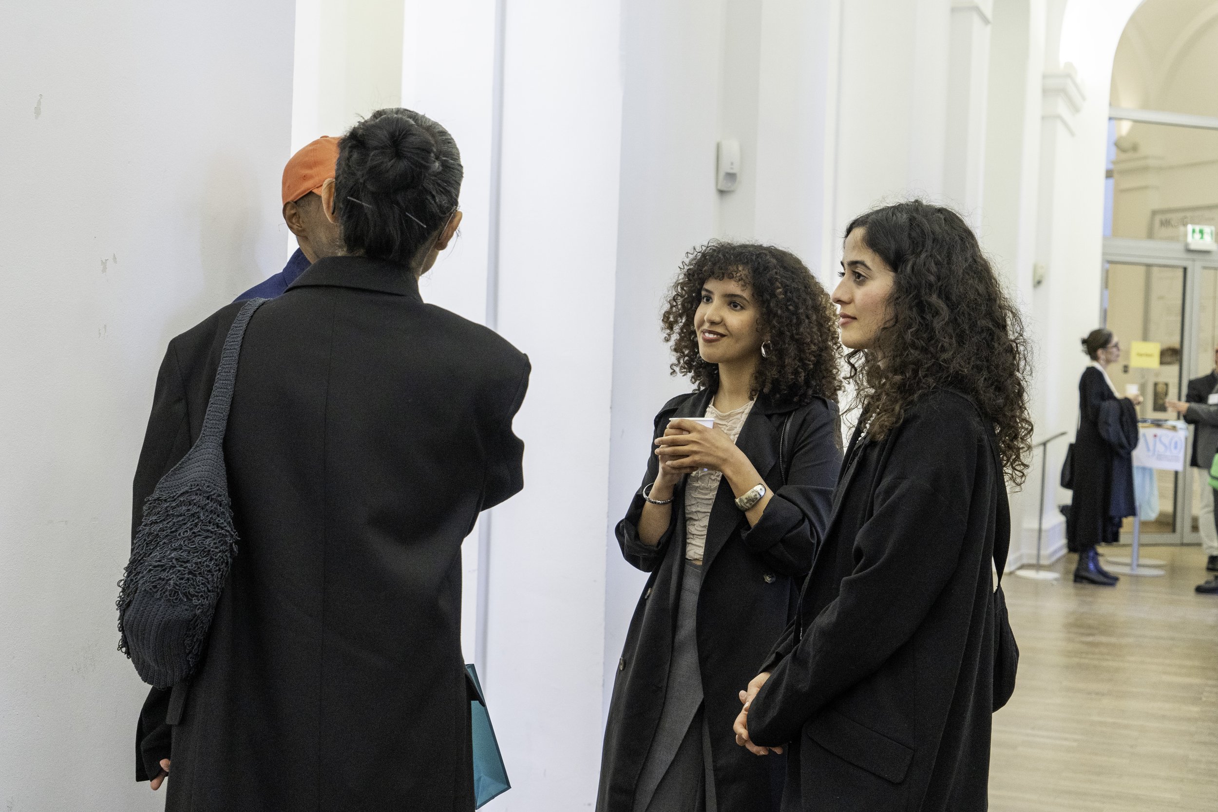 Drei Frauen im Gespräch auf einer Messe oder Konferenz, im Hintergrund weitere Personen und Messestände.