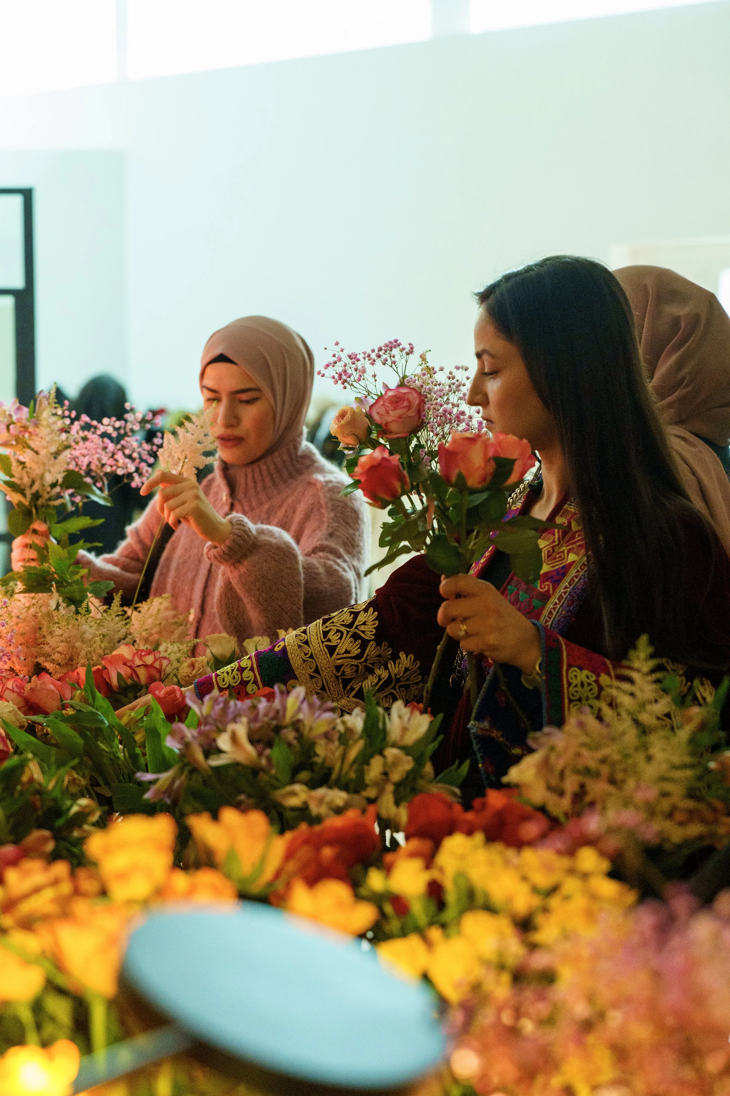 Drei Frauen, die an einem Blumenstand stehen und Blumen betrachten, mit vielen bunten Blumen vor ihnen.