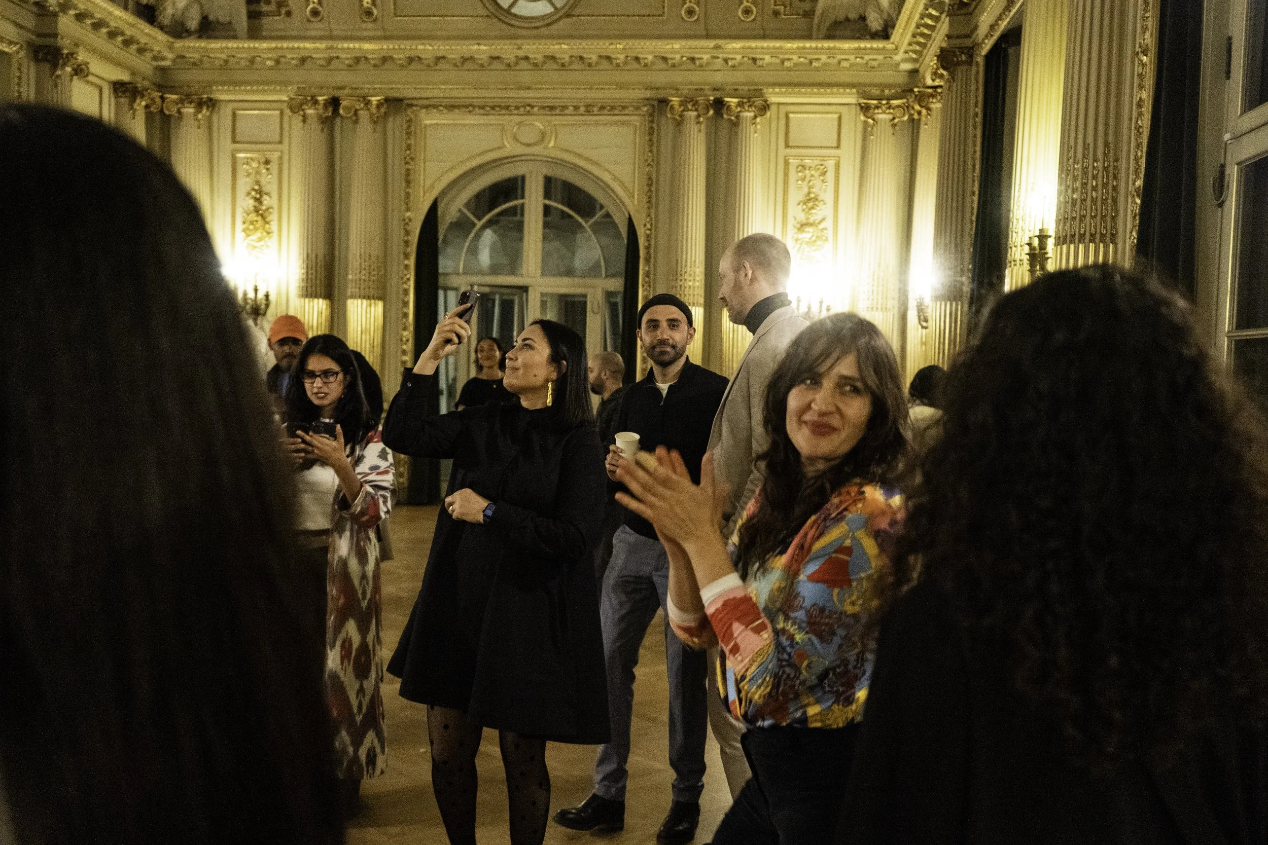 Menschen beim Feiern in einem elegant dekorierten Raum mit hohen Fenstern und goldverzierten Wänden.
