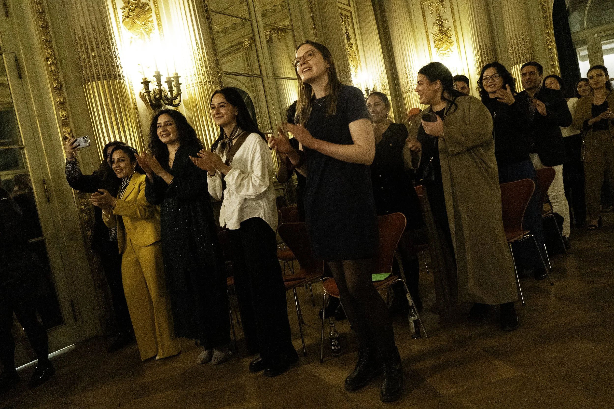 Gruppe von Menschen beim Applaudieren und Lachen in einem eleganten, goldverzierten Saal.