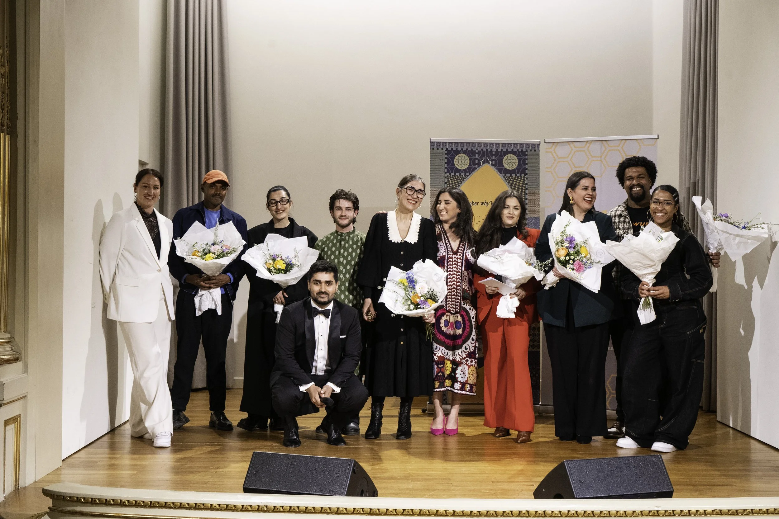 Gruppe von Menschen auf einer Bühne, die Blumen hält, bei einer Feier oder Zeremonie.