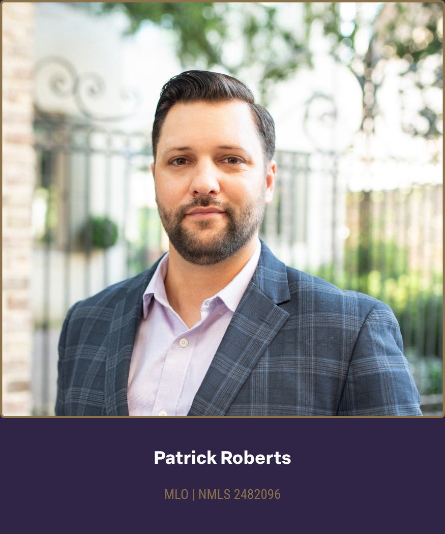 Professional headshot of Patrick Roberts in a business suit outdoors with a blurred background of trees and a wrought iron gate.