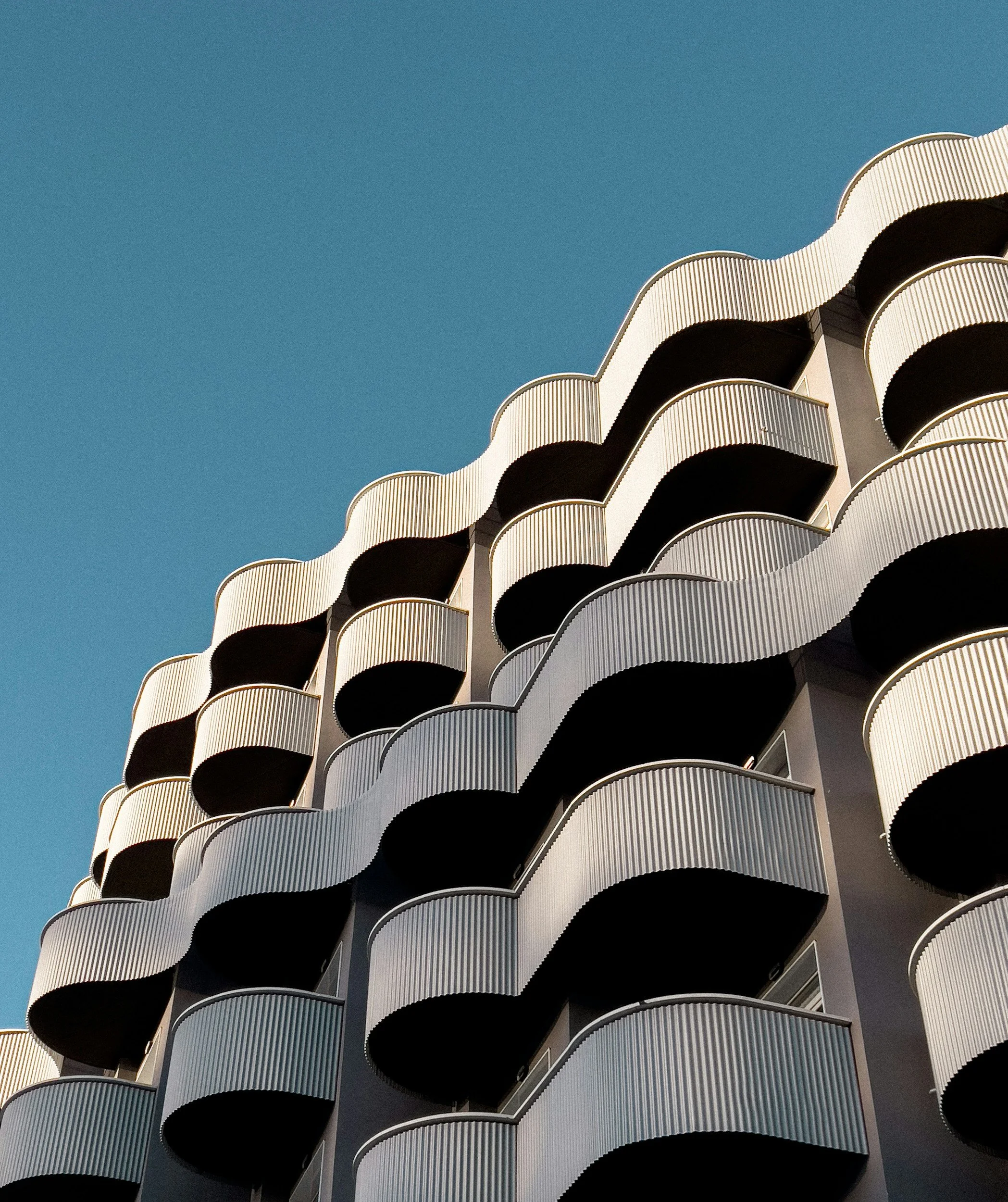 Modern building with wave-shaped balconies against a clear blue sky.