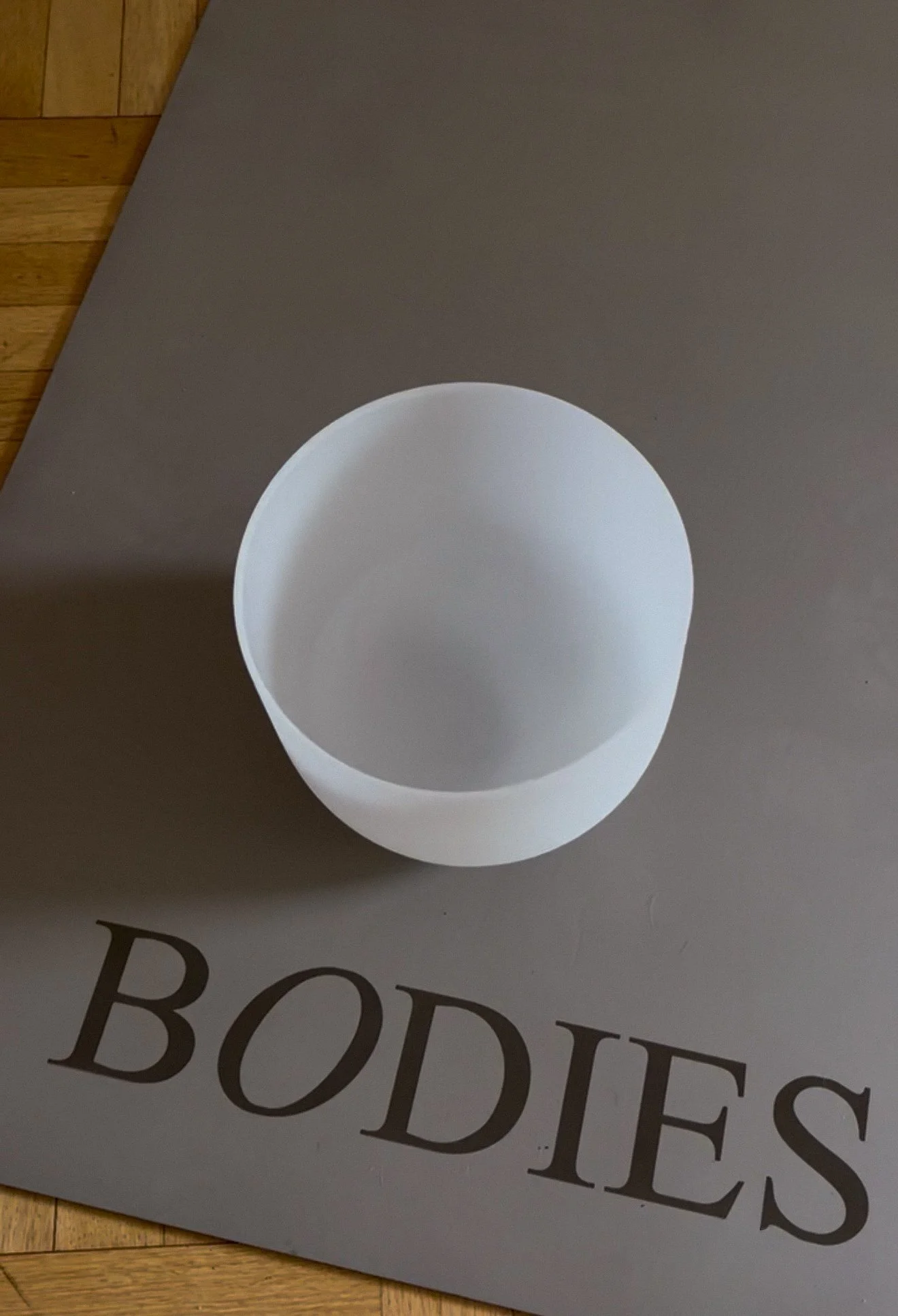 Empty white cup on a gray surface with a magazine underneath that reads 'BODIES'.