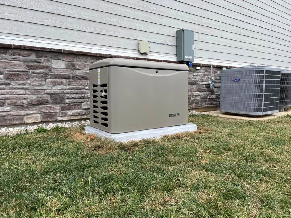 Outdoor HVAC units next to a house with a stone foundation and siding, on a grassy lawn.