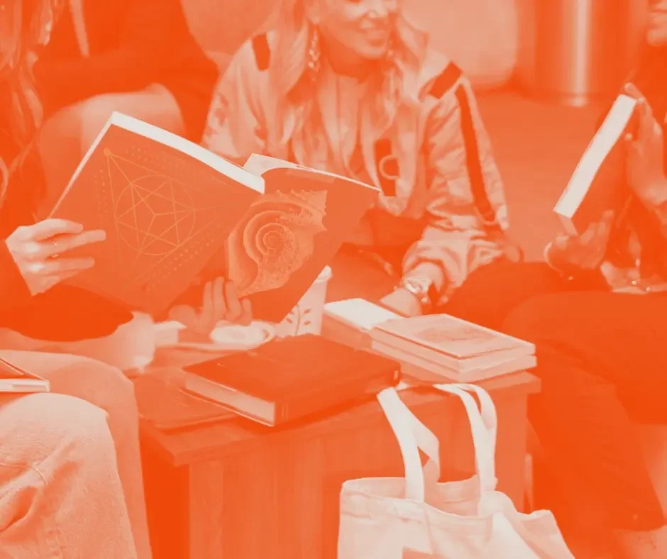 Group of people sitting on the floor with books and notebooks, engaged in reading or discussion.