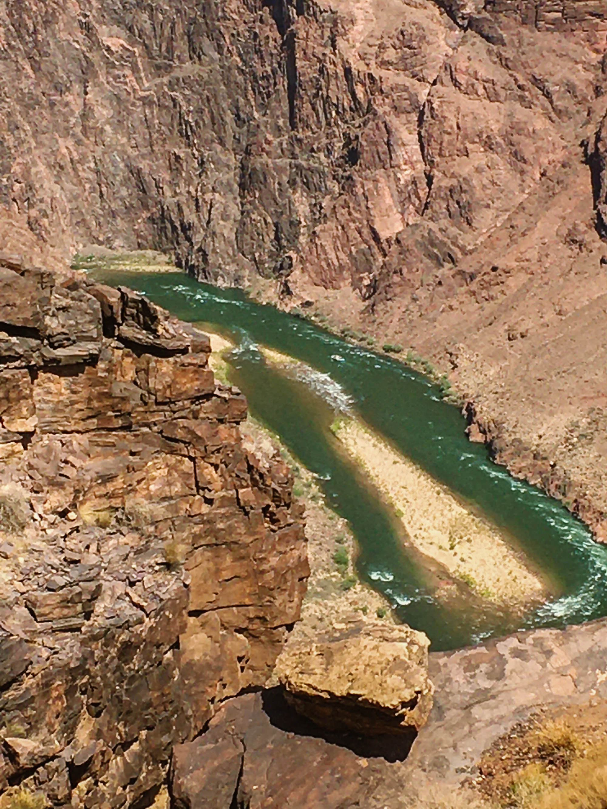 A river flowing through a canyon with high, rugged, reddish-brown rock walls.