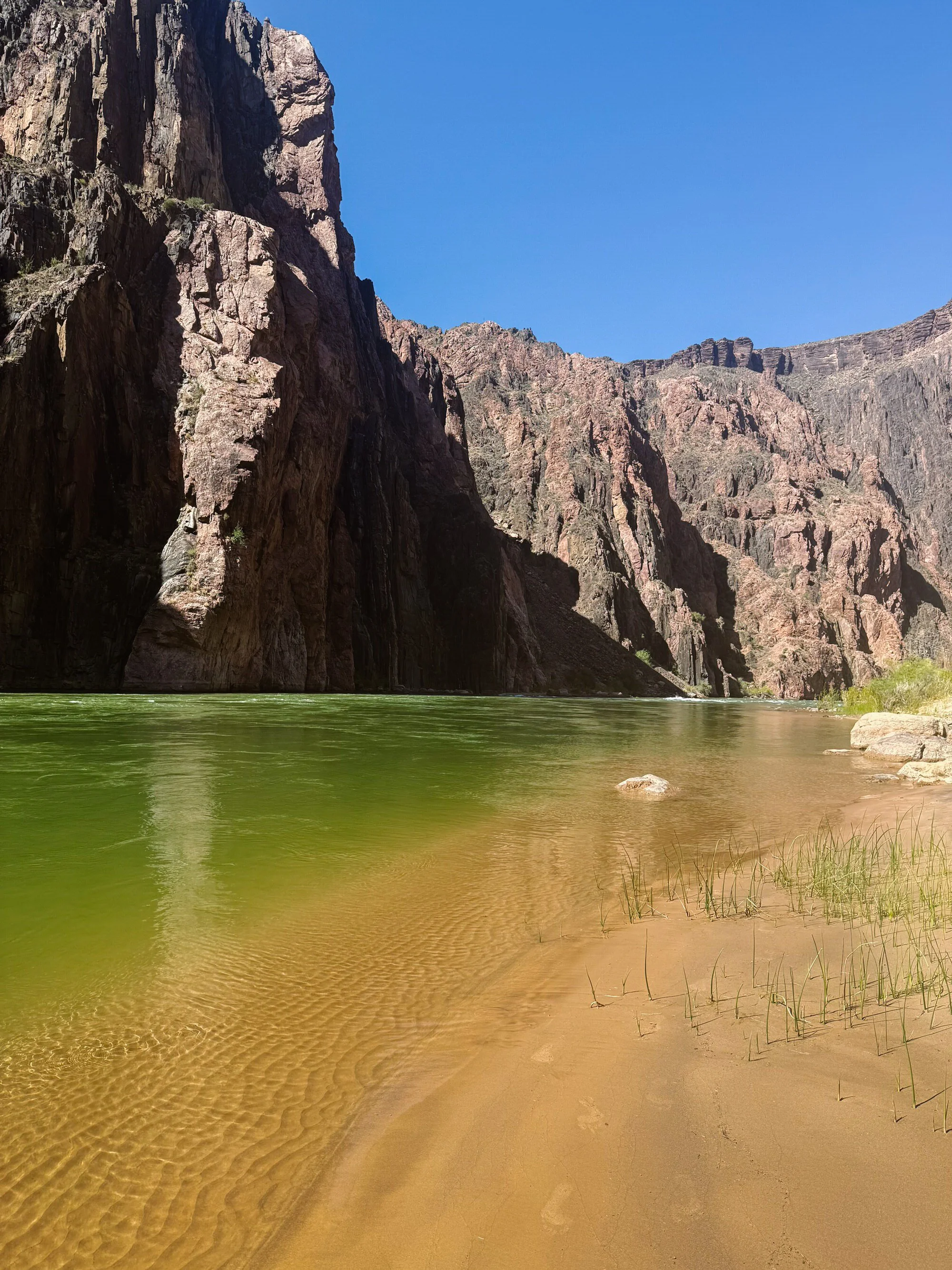 A river flowing through a canyon with steep rocky cliffs and a clear blue sky.