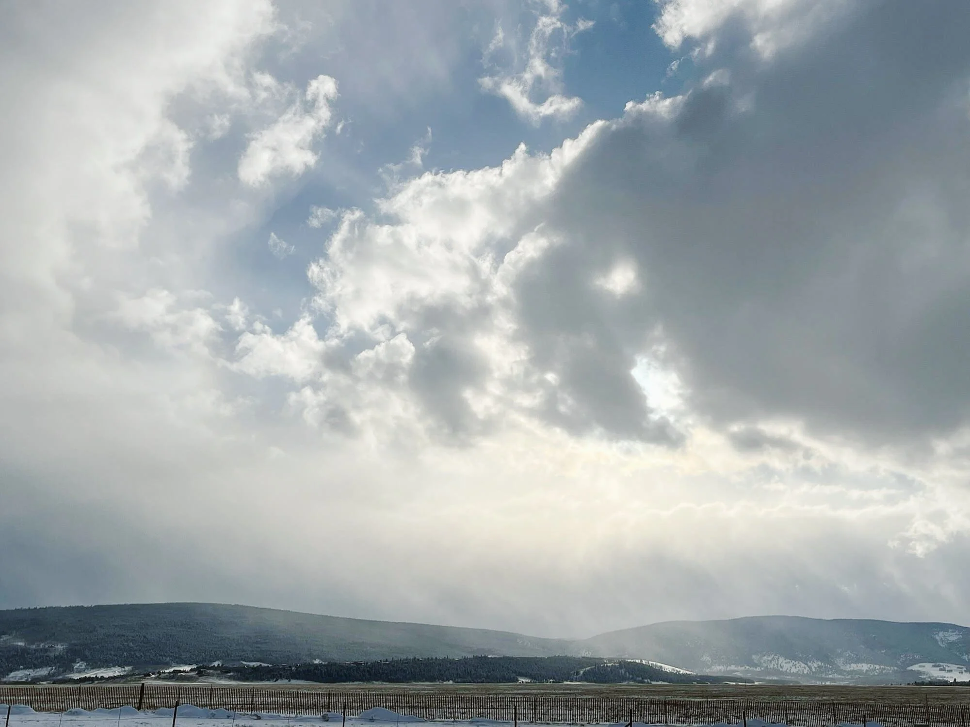 A panoramic view of a mountain range under a cloudy sky with patches of sunlight breaking through.