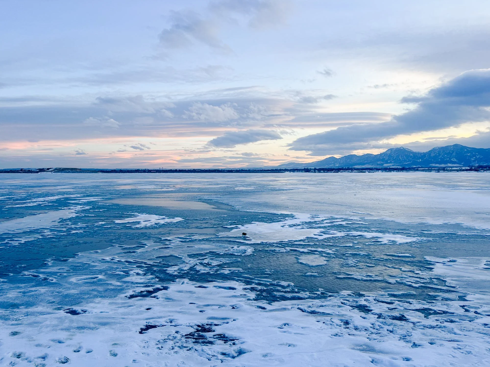 Frozen body of water with a mountain range in the distance under a cloudy sky
