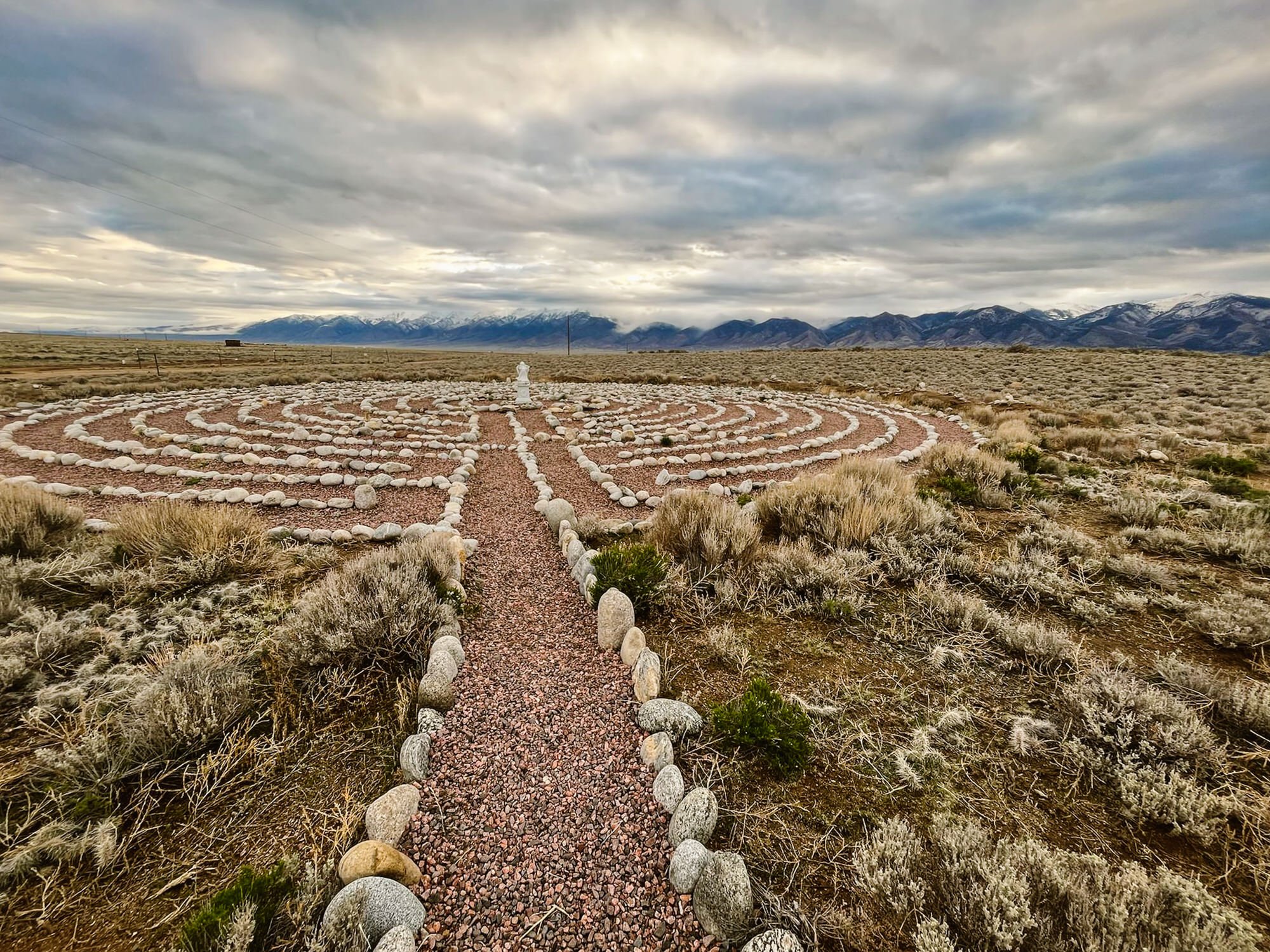 A pentagram-shaped rock formation in a desert landscape with mountains in the background and cloudy sky above.