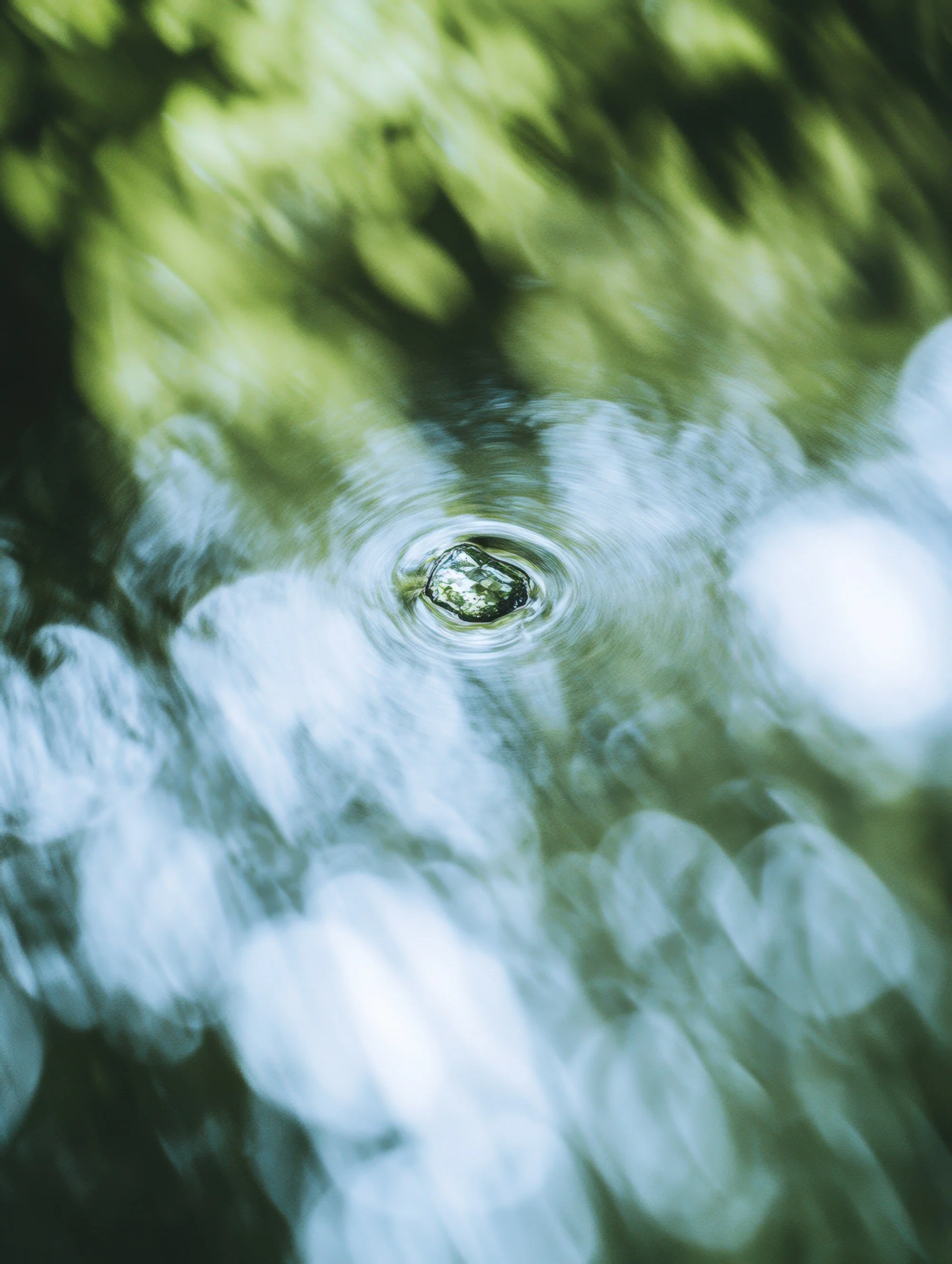 A close-up view of water ripples on a flowing stream with green foliage reflected on the surface.