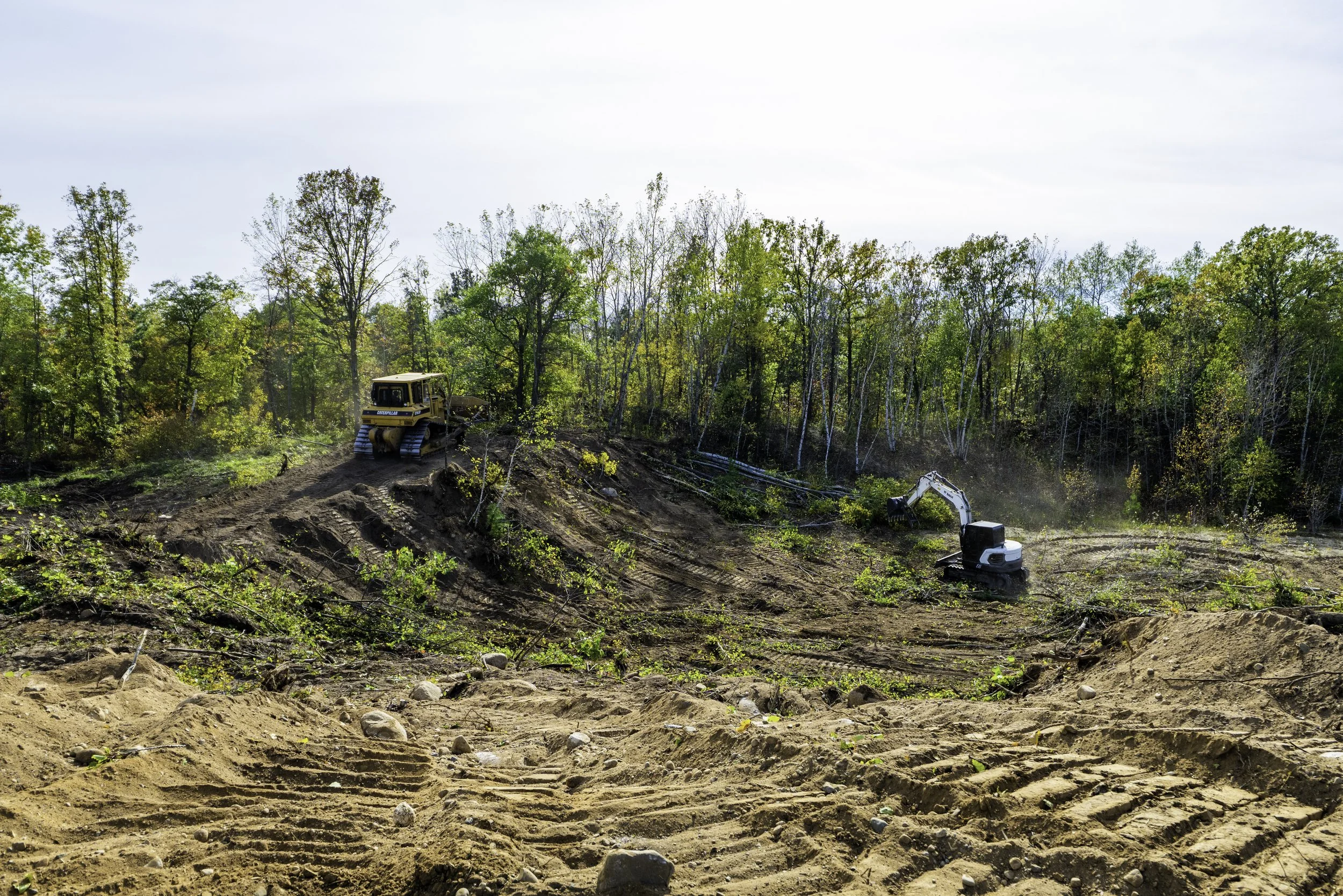 Construction site with bulldozer and excavator working on clearing land among trees.
