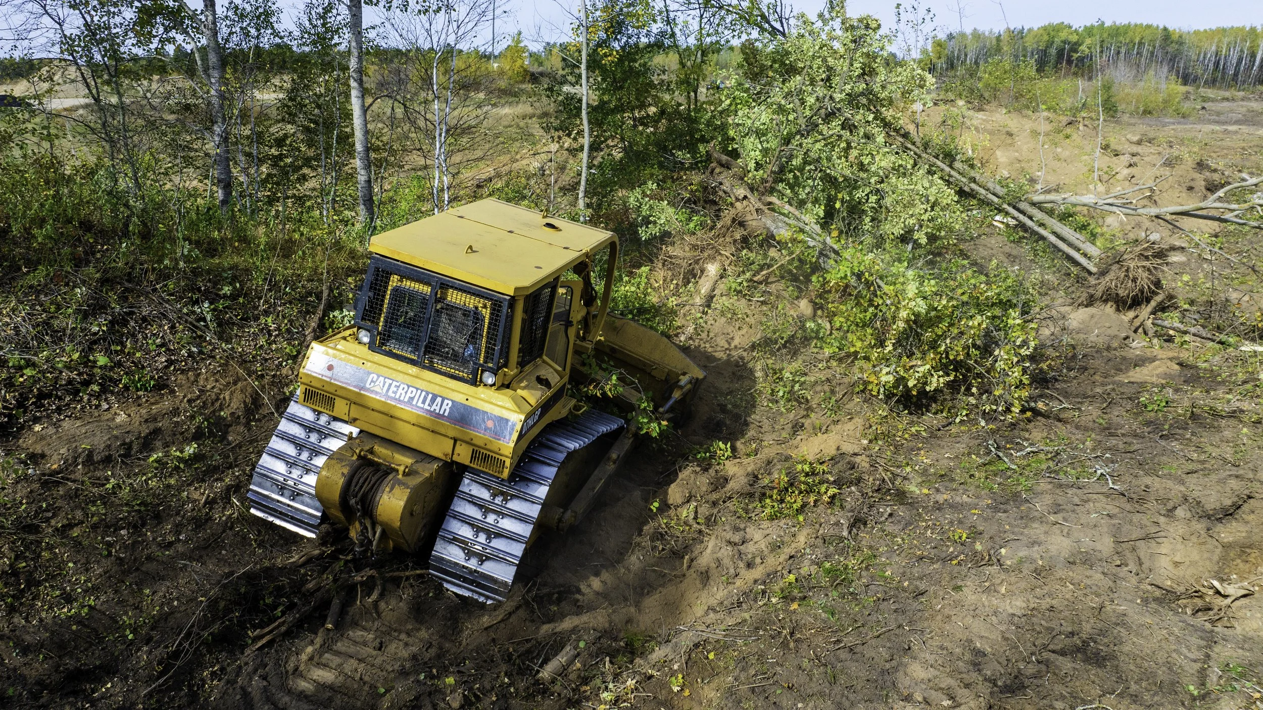 A yellow Caterpillar bulldozer moving soil and clearing land in a forested area