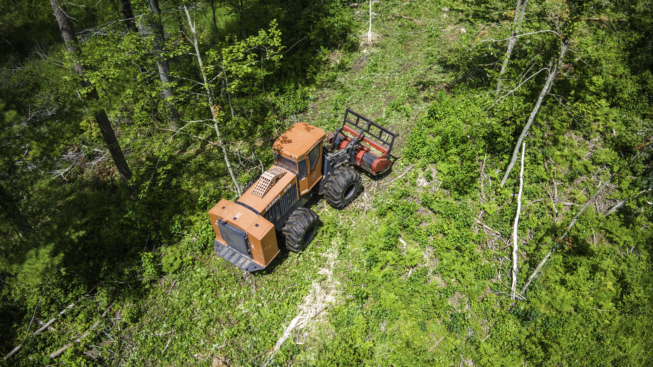 An orange tractor working on a forested area, viewed from above.