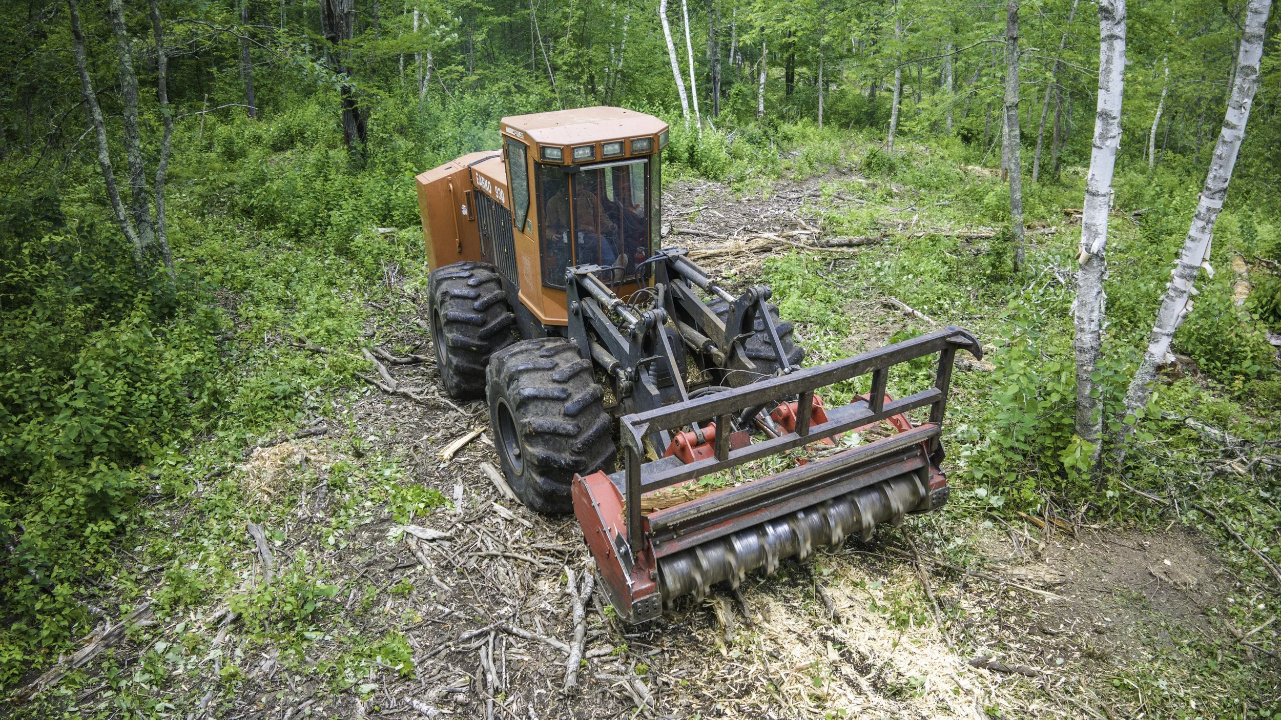 A bulldozer with large tires and an orange body working in a forest clearing.