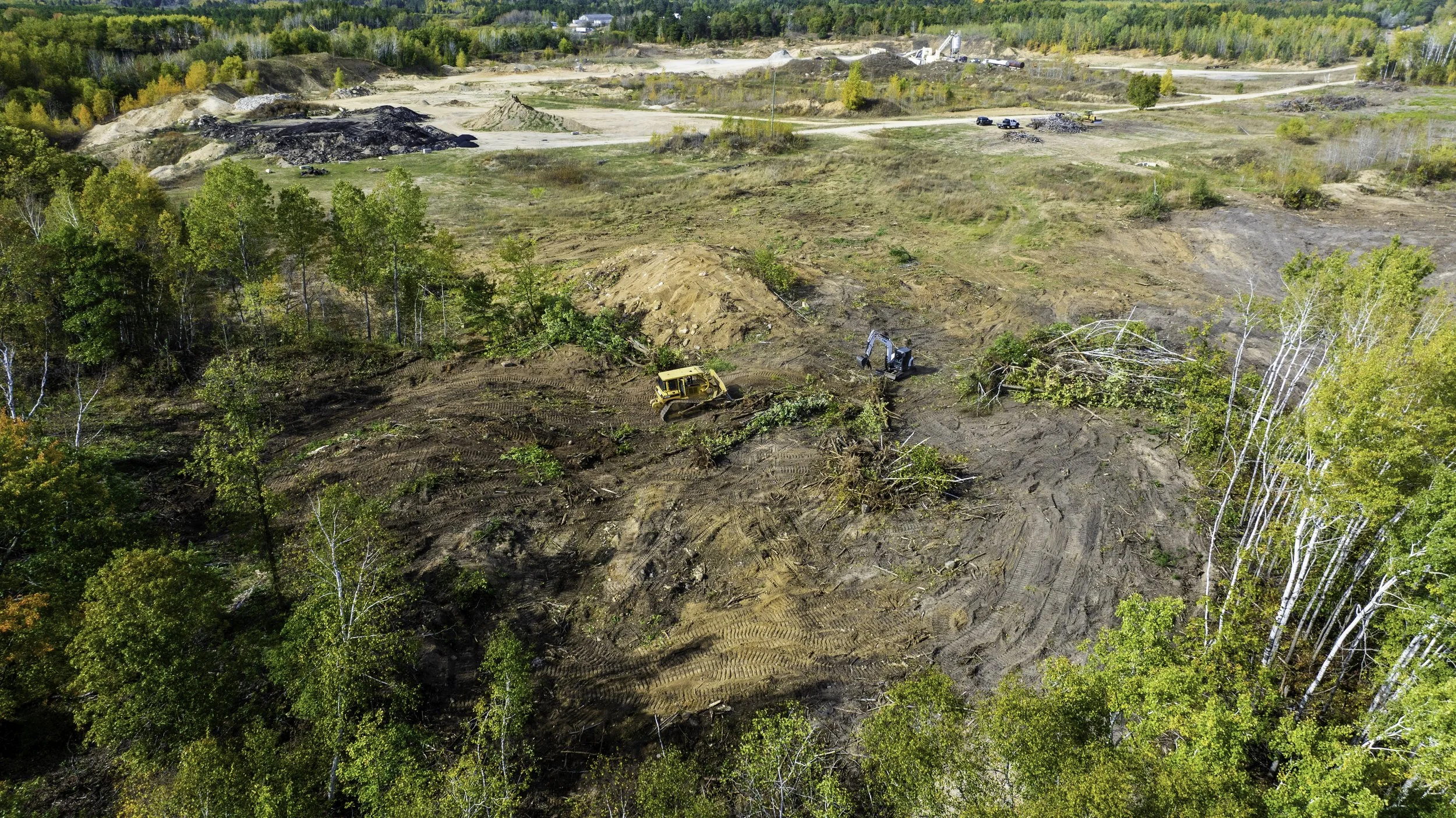 Aerial view of a construction site in a forested area with heavy machinery clearing trees and preparing land for development.