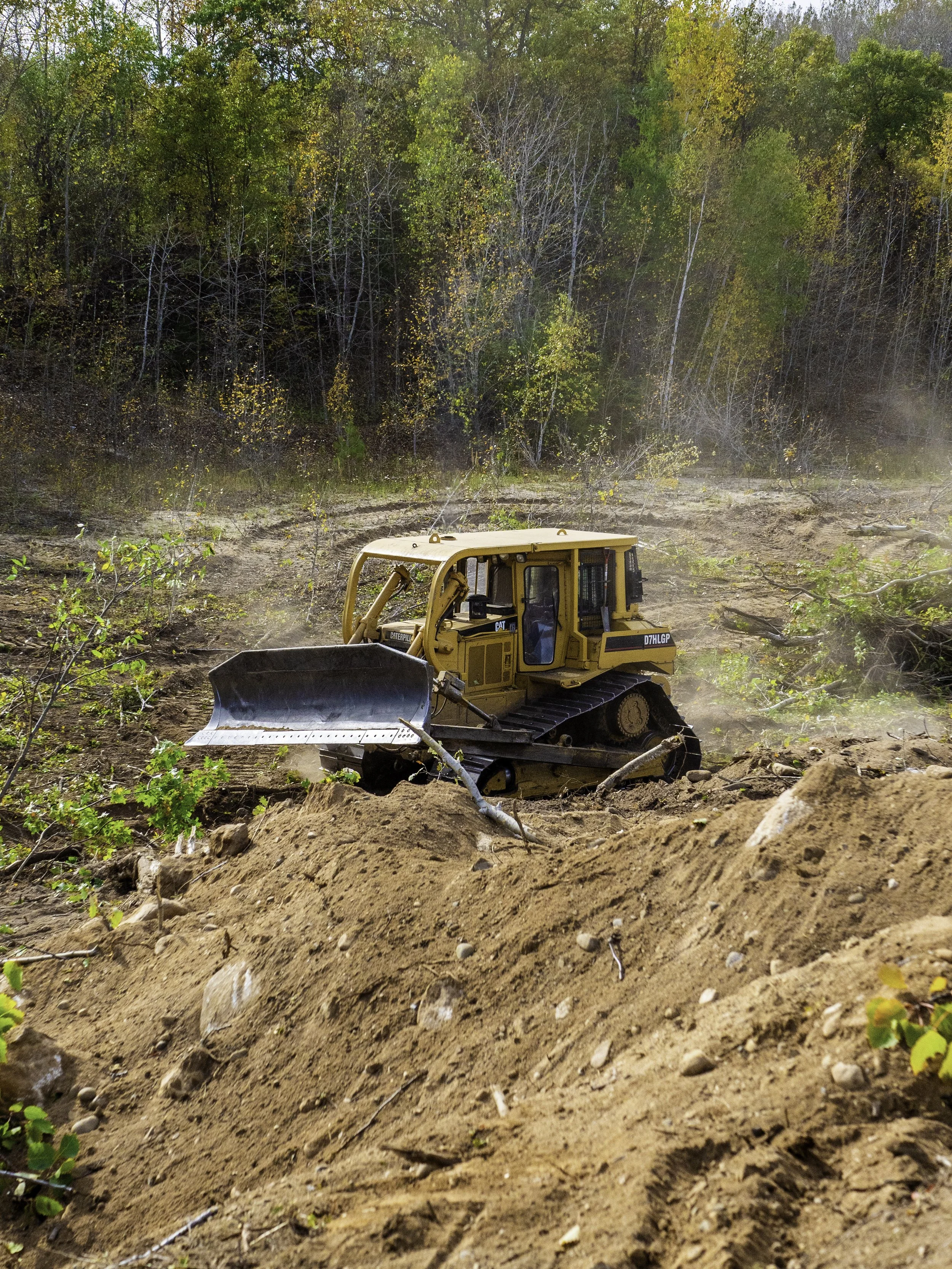 A yellow bulldozer working on a dirt clearing in a forested area during daytime.