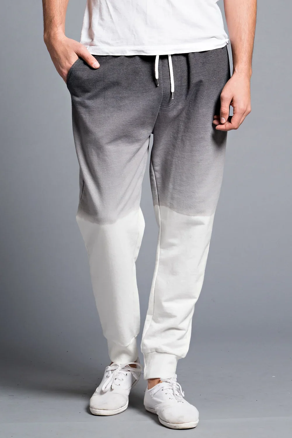 A person wearing gradient gray to white sweatpants, a white T-shirt, and white sneakers.
