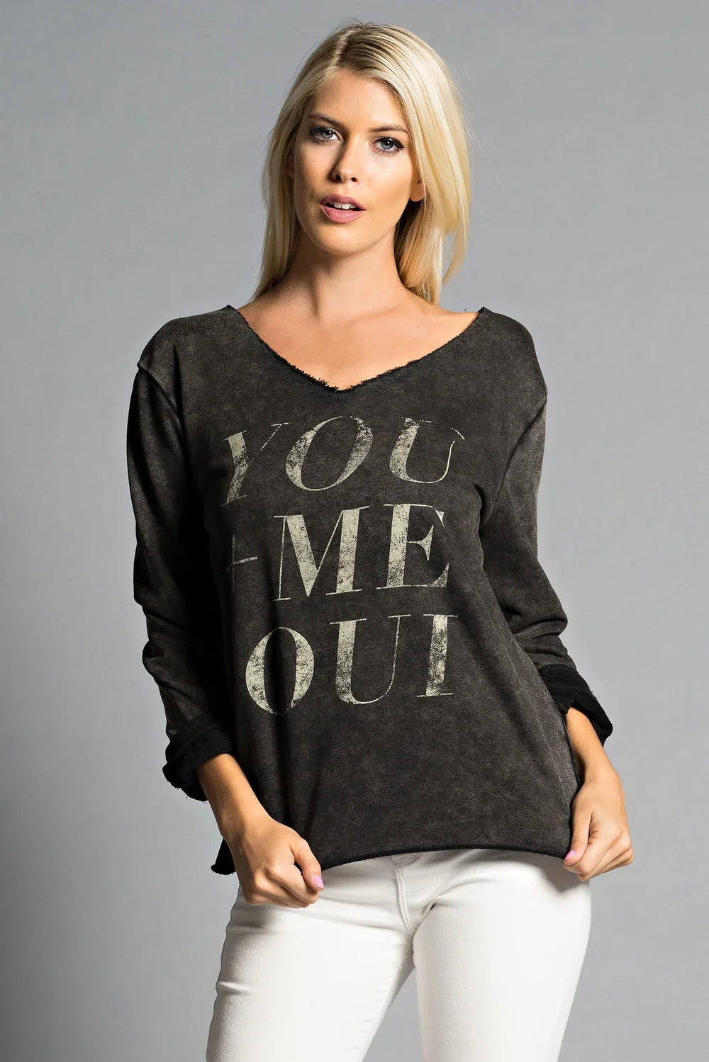 A woman with blonde hair wearing a dark gray long-sleeve shirt with the words "You Love Me Out" in large printed letters, standing against a gray background.
