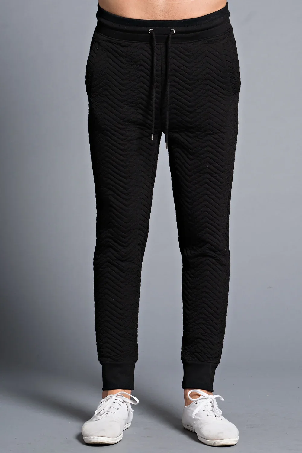 Person wearing black quilted jogger pants with white sneakers standing against a neutral background.