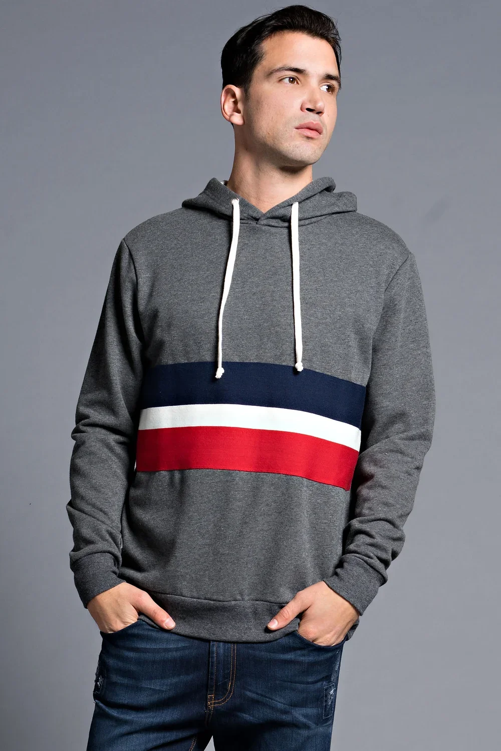 Man in a gray hoodie with navy, white, and red stripes, standing against a gray background.