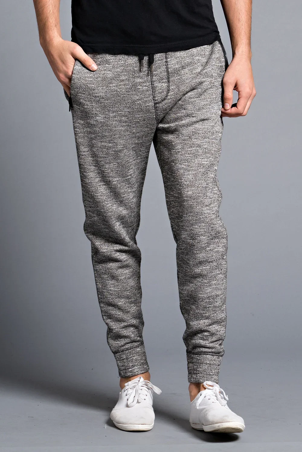 Person wearing gray casual jogger pants, white sneakers, and a black T-shirt, standing against a gray background.