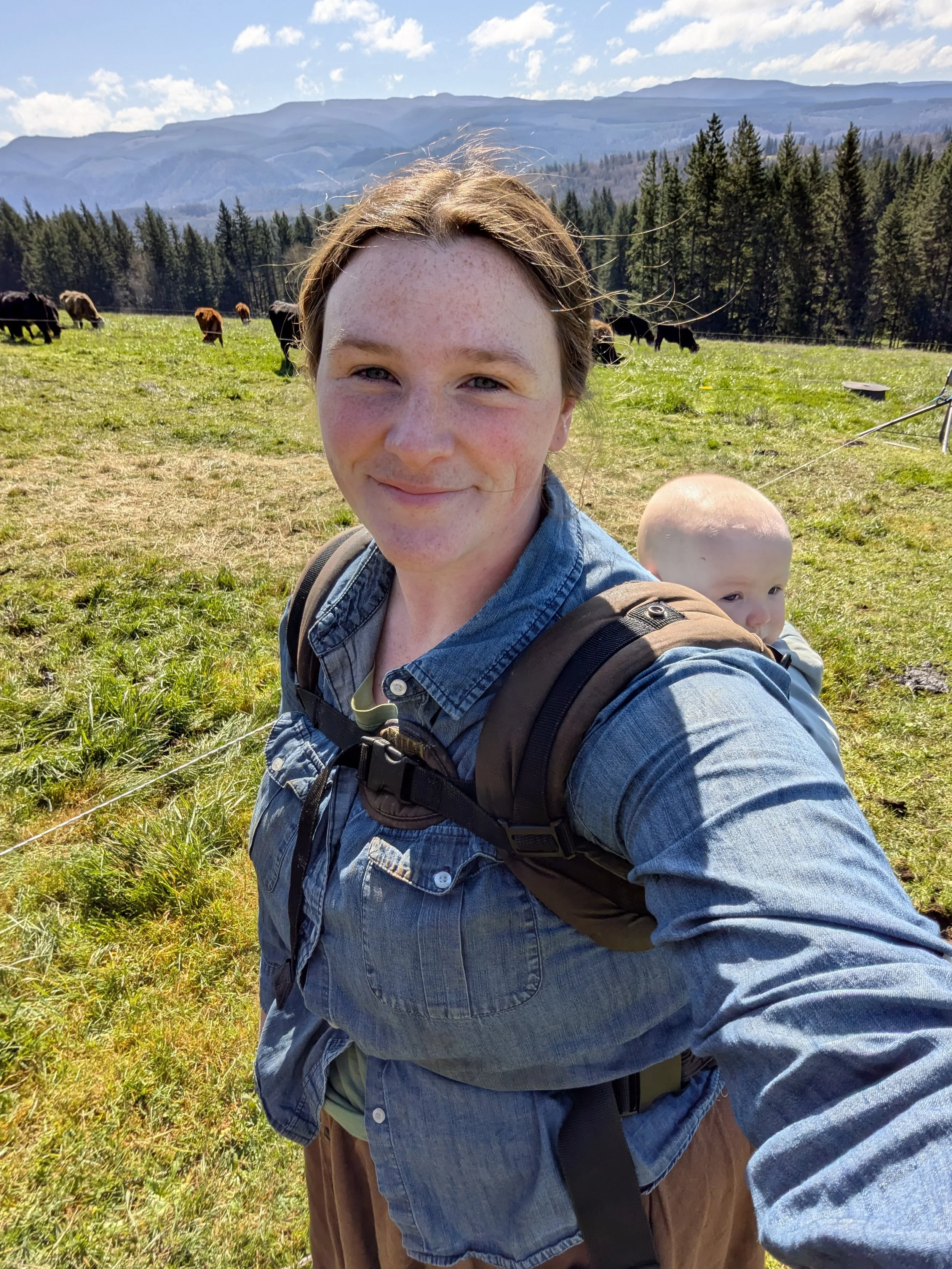 woman with baby in front of herd of grass fed cows