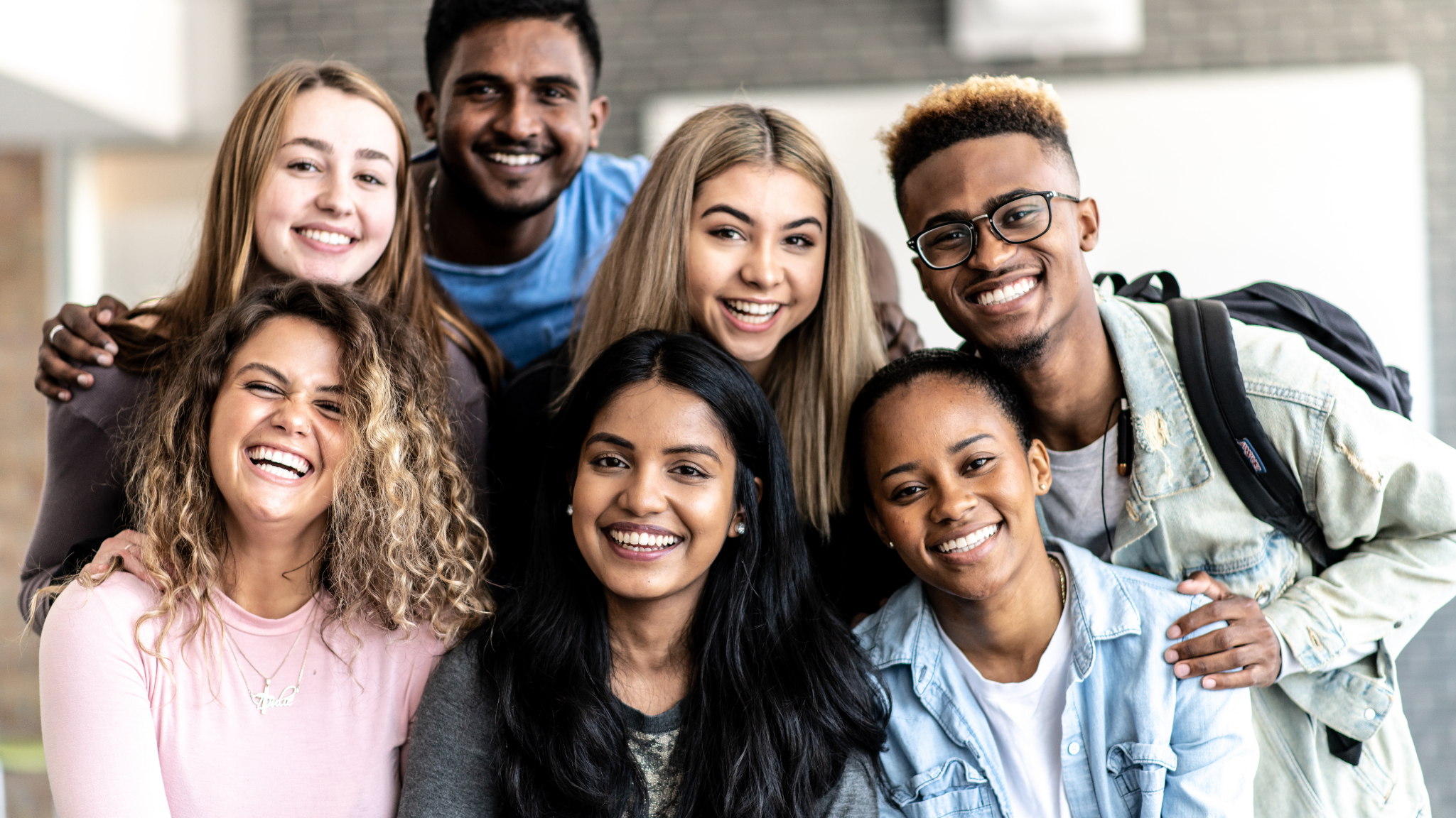 Group of smiling young people posing indoors in a close group, diverse in ethnicity and appearance.