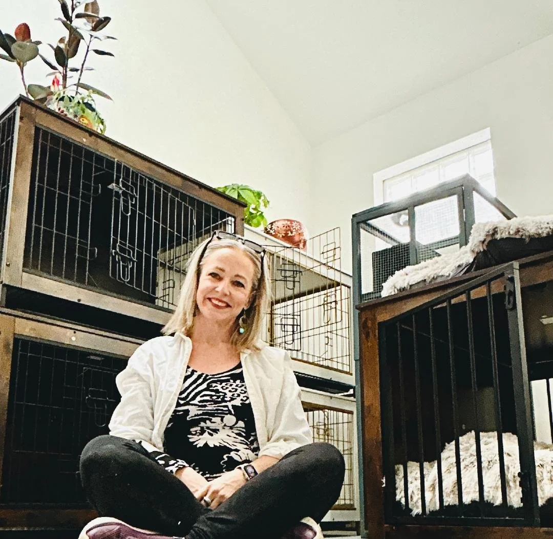 A smiling woman sitting cross-legged inside a room with pet cages and plants in the background.