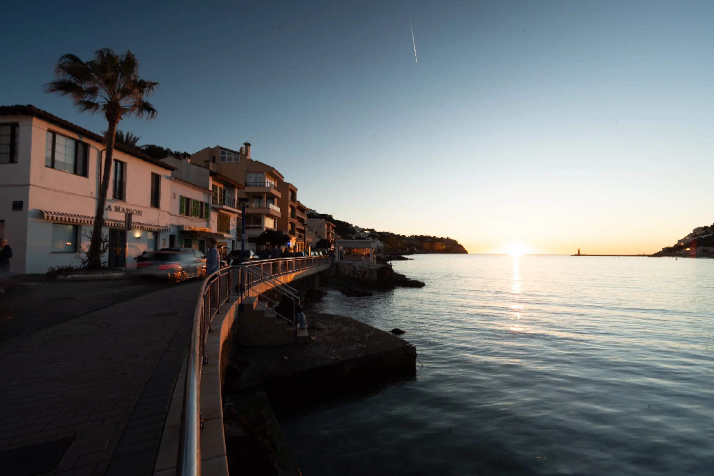 Sunset over the water in a coastal town with buildings, palm trees, and a seawall