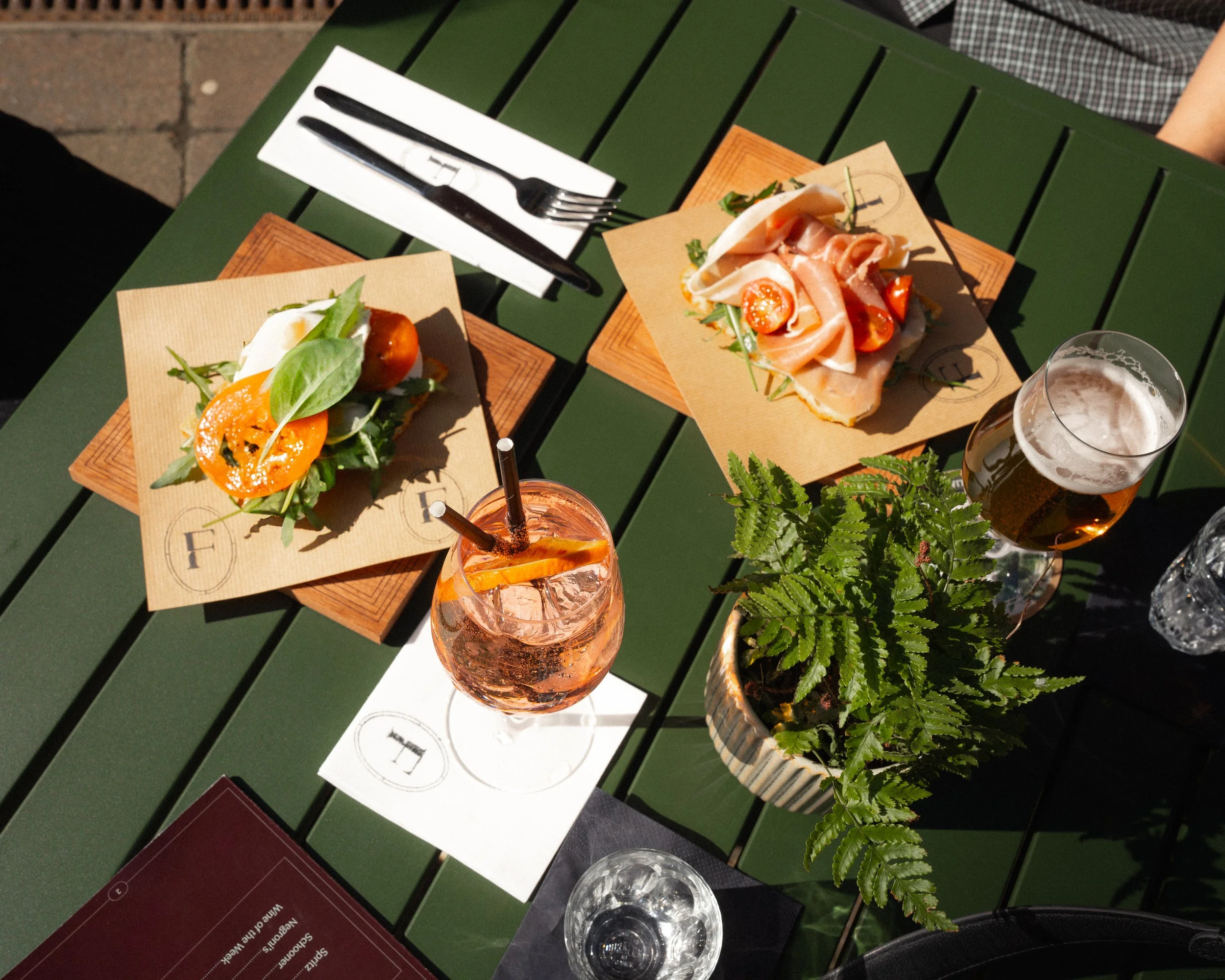 Outdoor table with two plates of salad and drinks, a potted fern plant, and utensils, taken from an overhead perspective.