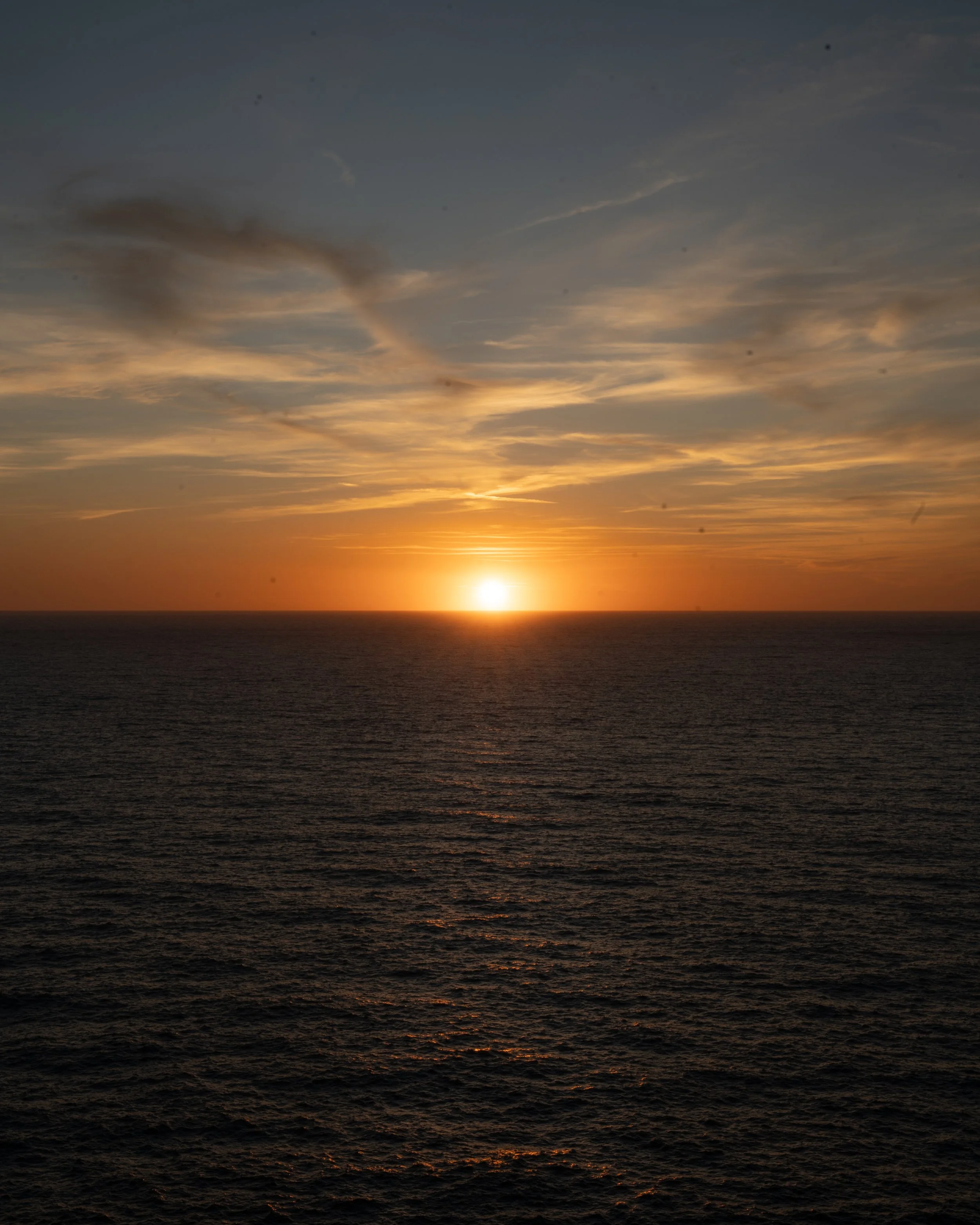Sunset over the ocean with orange and yellow hues in the sky and dark water below.