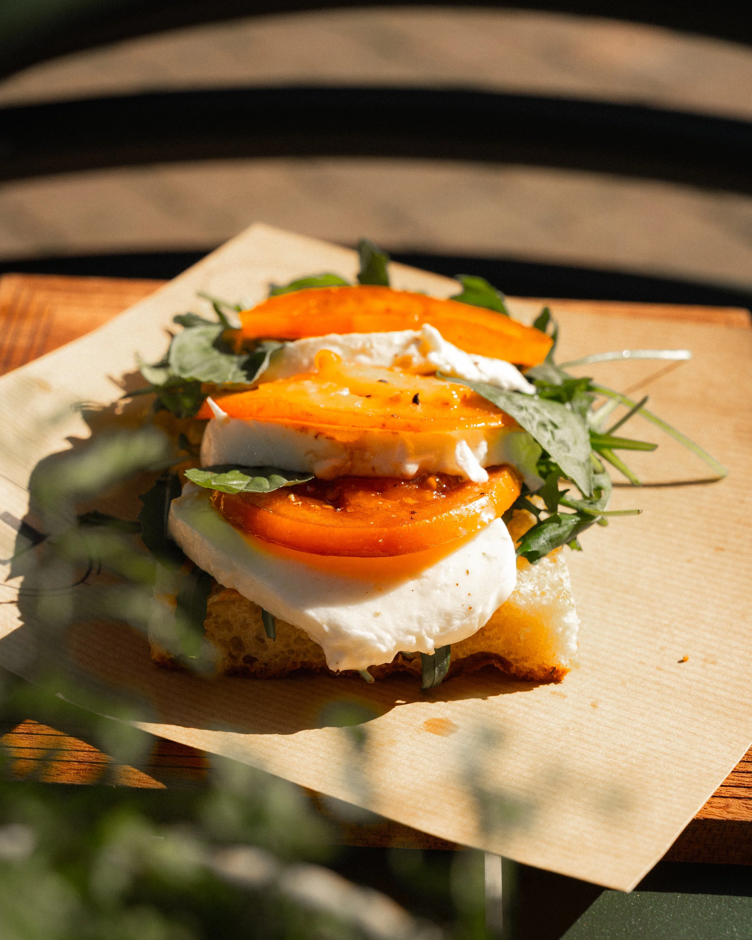 A piece of toast topped with sliced tomatoes, fresh greens, and two poached eggs, garnished with black pepper.