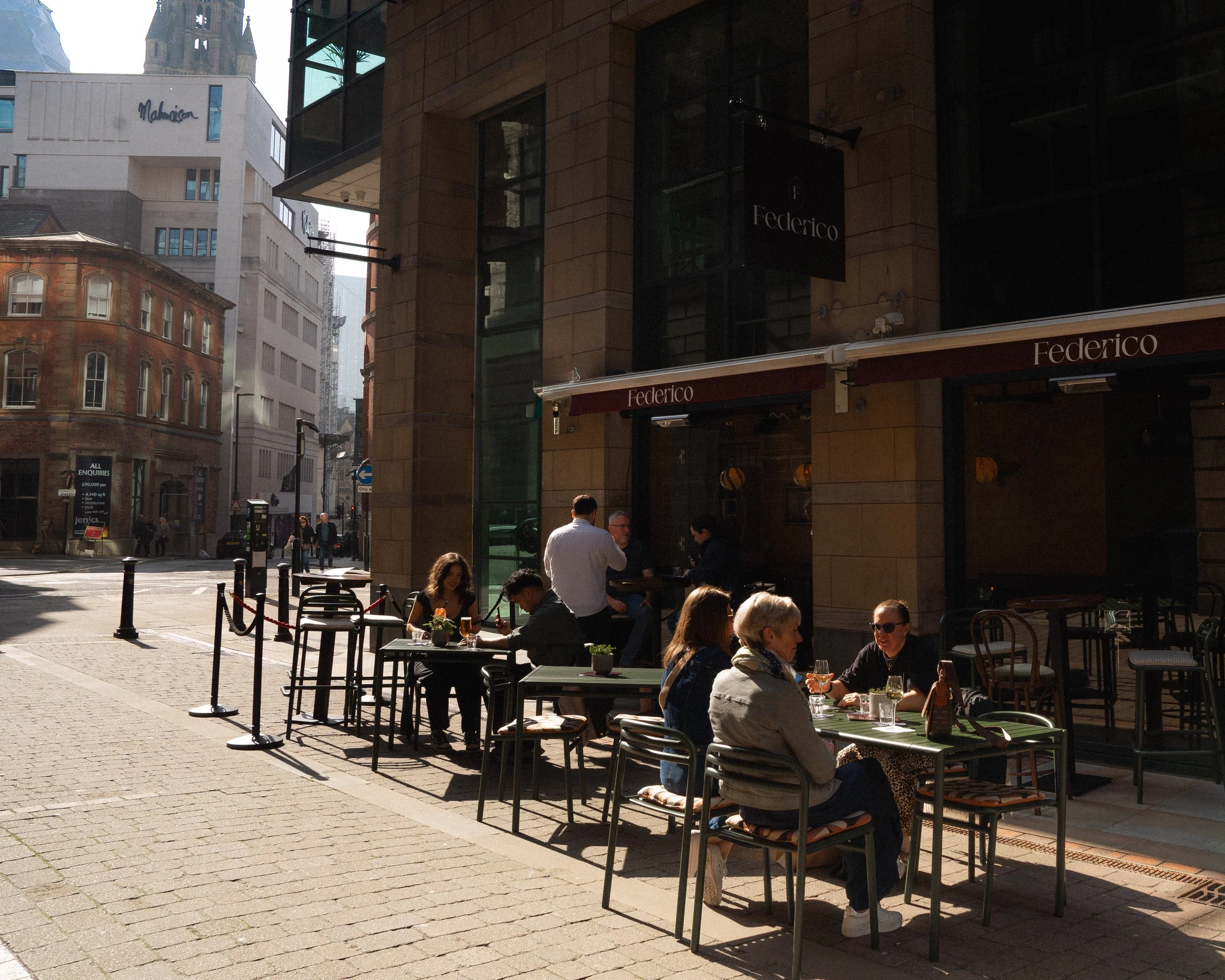 People dining at outdoor tables in front of a restaurant called Federico on a city street, with buildings and pedestrians in the background.